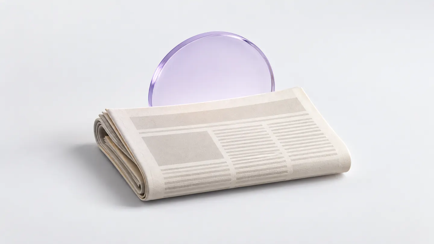 A folded ivory newspaper in front of a lavender glass sunrise disc.